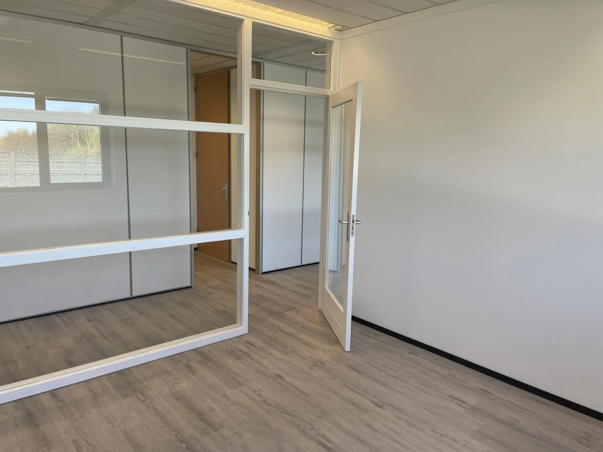 Licht en modern kantoorpand aan de Laan van s-Gravenmade met glazen tussenwand, openstaande deur en laminaatvloer.